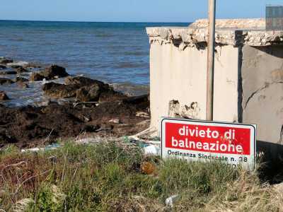 Inghiottito dall�erba e dalle bottiglie di plastica si trova poi un cartello che segnala il divieto di balneazione